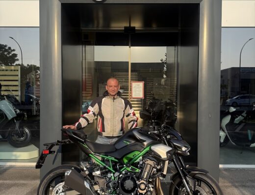 Un uomo posa con una moto Kawasaki di fronte al negozio 4 Tempi Moto Store. Accessori e abbigliamento moto disponibili.