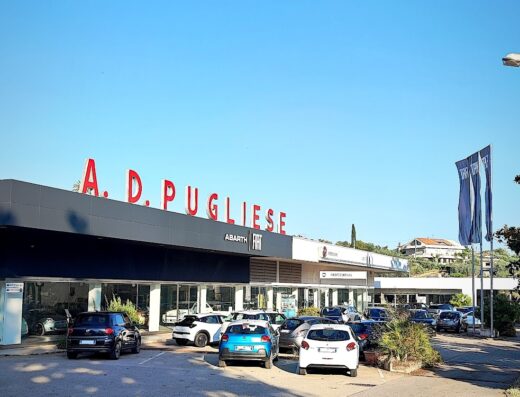 A.D. PUGLIESE S.p.A. concessionaria auto con diverse auto parcheggiate di fronte all'edificio in una giornata assolata.