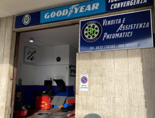 A.M. Gomme tire shop exterior in Italy, featuring Goodyear signage, tire sales and service, wheel alignment, tire stacks, and a 'no parking' sign.