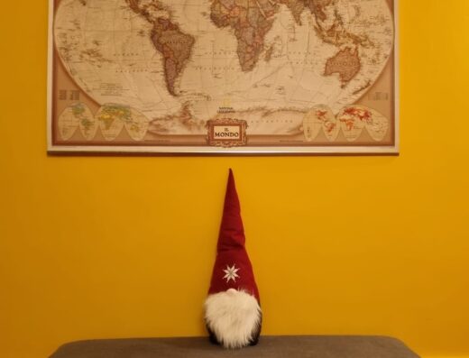 Mappa del mondo vintage appesa sopra una panca grigia con uno gnomo decorativo, ideale per la pianificazione di progetti di viaggio con A.PI Studio.