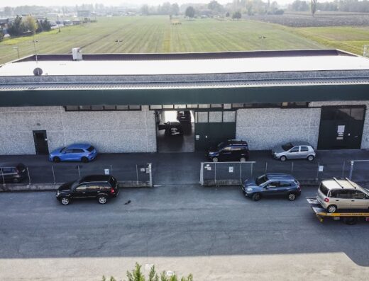 AB Motor Srl: Vista aerea dell'officina con auto parcheggiate, alcune in riparazione e un carro attrezzi. Servizi di riparazione auto e moto.