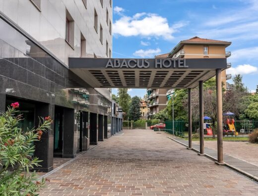 Ingresso dell'Abacus Hotel con pavimentazione in mattoni, insegna ben visibile e parte dell'edificio moderno sullo sfondo.