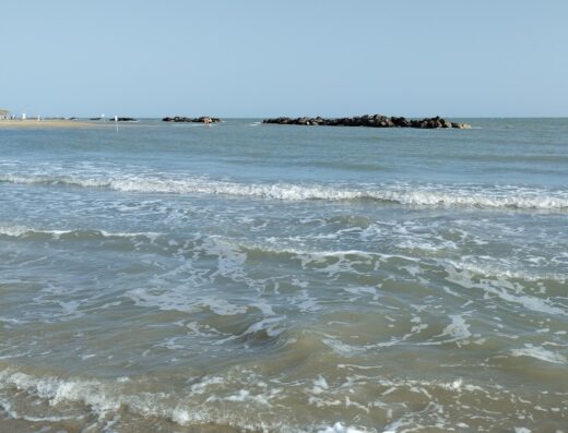 Vista mare con onde che si infrangono sulla spiaggia, scogli in lontananza sotto un cielo sereno. Abruzzo Motor Show.
