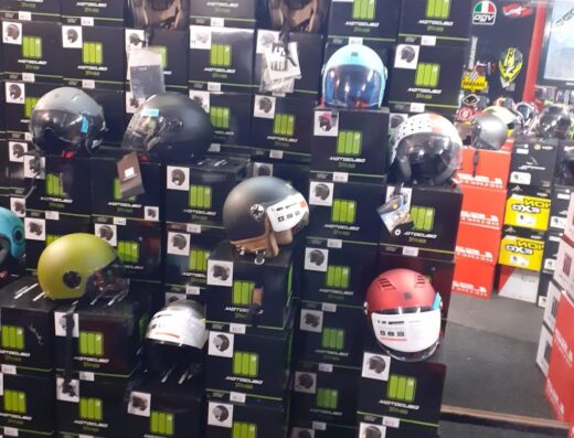 Esposizione di caschi da moto di vari colori e modelli, impilati sopra le loro scatole marchiate Motoclub, in un negozio di accessori per motociclisti.