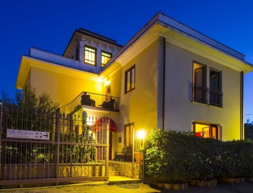 Foto notturna dell'Affittacamere Villa Margherita, una struttura ricettiva con balcone e insegna indicativa per i viaggiatori in moto e auto.