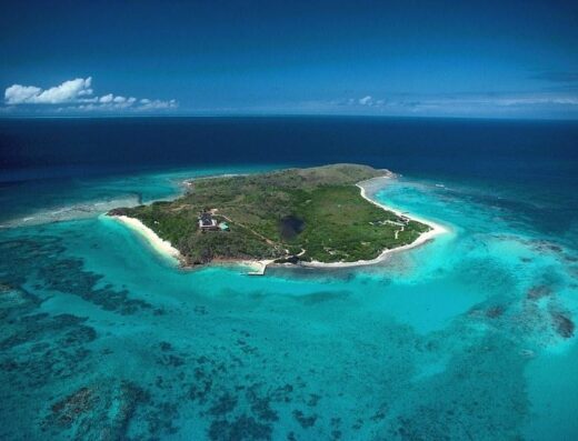 Vista aerea di un'isola tropicale con vegetazione lussureggiante, spiagge bianche e acque turchesi cristalline, ideale per viaggi e vacanze esclusive.
