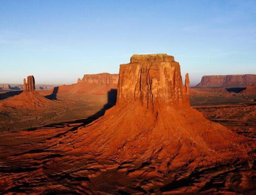 Monument Valley in Arizona, a sandstone landmark with towering buttes against a clear blue sky, a popular travel destination.