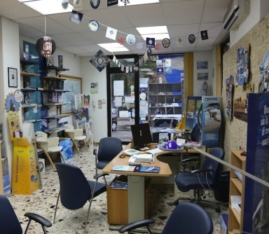 Interni dell'Agenzia Viaggi Adacta Travel, con scrivania, sedie, scaffali con offerte di viaggio e decorazioni festive.