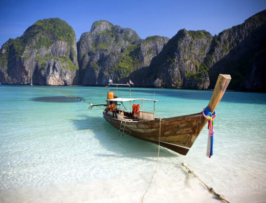 Imbarcazione tradizionale thailandese ormeggiata su una spiaggia di sabbia bianca con acque cristalline e scogliere calcaree sullo sfondo, ideale per escursioni e viaggi in Molise