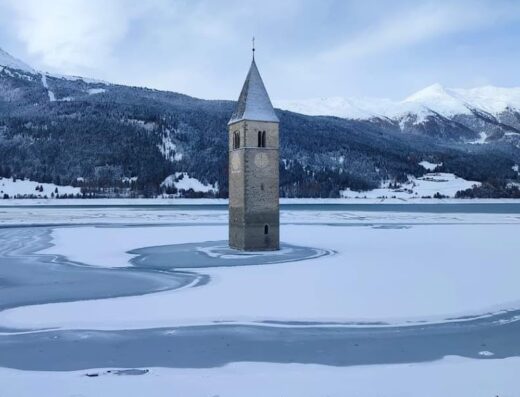 Il campanile sommerso del Lago di Resia in inverno, una meta turistica unica per viaggi e avventure in moto attraverso paesaggi innevati.