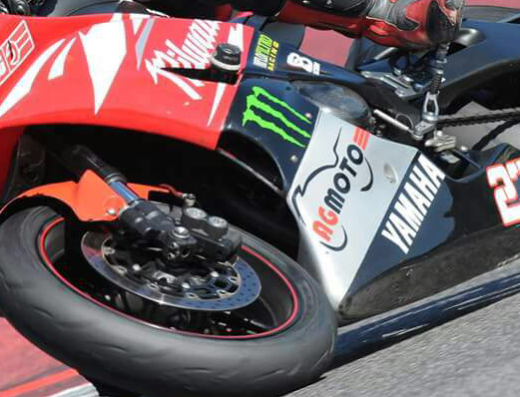 AGmoto Pavia: Dettaglio di una moto Yamaha da corsa in pista, con pneumatici performanti e livrea personalizzata. Accessori e dettagli di alta qualità per appassionati di motociclismo sportivo.