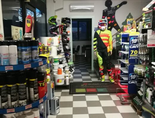 Interno del negozio Agosti S.R.L. Ricambi Auto e Moto con scaffali di accessori moto, caschi, vernici e un manichino con abbigliamento da motocross.