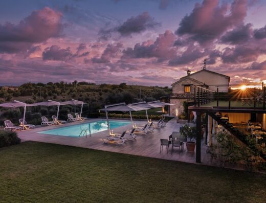 Agrirelais Collelago: piscina illuminata al tramonto con lettini e ombrelloni, prato curato, atmosfera rilassante per motociclisti in viaggio.