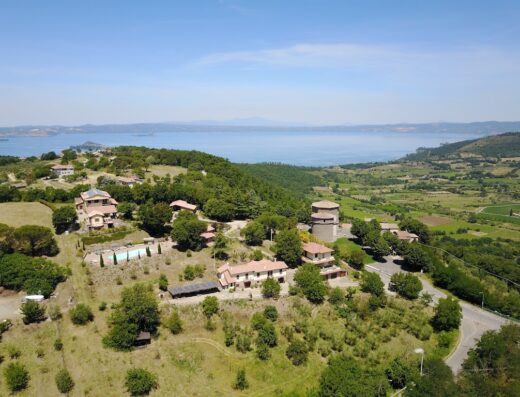 Vista aerea di AgriResort & Glamping SPA Poggio di Montedoro con piscina, lago sullo sfondo e paesaggio collinare.