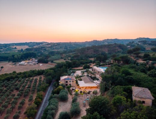 Vista aerea dell'Agriresort Leano al tramonto, immerso nel paesaggio collinare laziale. Uliveto, piscina e illuminazione esterna creano un'atmosfera rilassante per viaggi e vacanze.