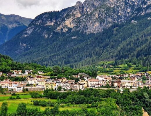 Paesaggio pittoresco di Agritur Al Molin, con vista sulle Dolomiti, boschi verdi e case tradizionali. Ideale per un viaggio in moto tra la natura.
