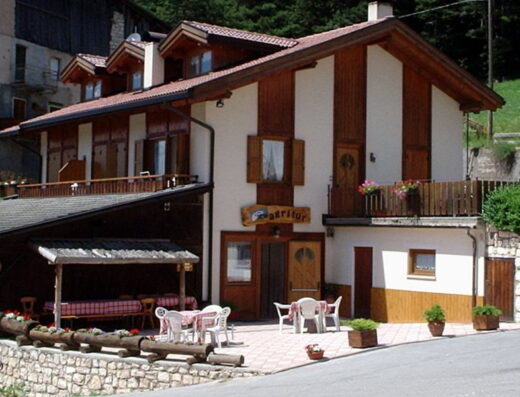 Agritur al Ranch Maso Coflari: Facciata esterna dell'agriturismo con tavoli apparecchiati all'aperto, balconi fioriti e dettagli in legno tipici della zona.