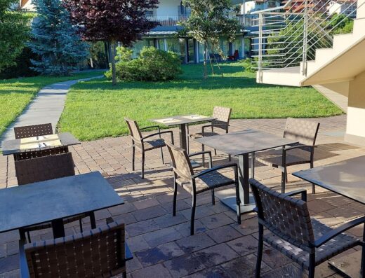 Outdoor seating area at Agritur Ponte Alto featuring tables and chairs on a patio with a view of the garden and surrounding buildings.