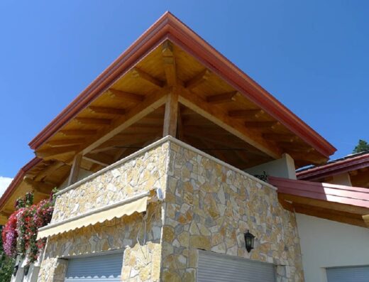 Struttura in legno e pietra dell'Agritur Vista Lago, con balcone fiorito e tenda parasole, dettaglio dell'architettura esterna.