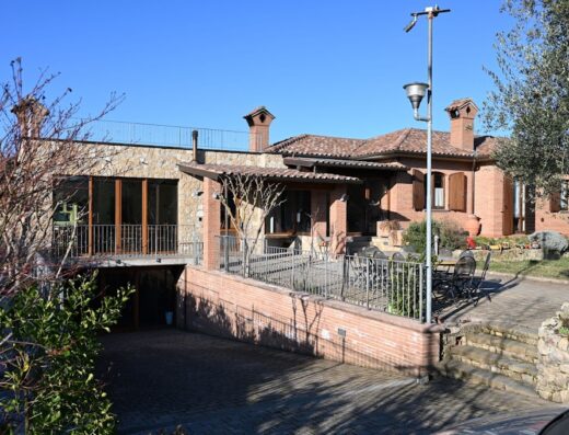 Esterno dell'Agriturismo A Casa Mia a Gubbio, Umbria, con facciata in pietra, tetto in tegole rosse, area esterna con tavolo e sedie, e accesso al garage.