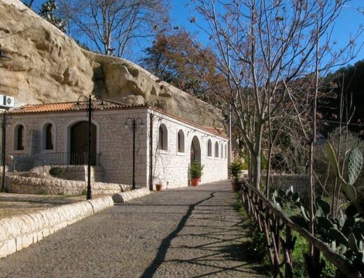 Agriturismo A'Cunziria: Vista esterna dell'agriturismo con facciata in pietra chiara, tetto in tegole rosse, sentiero acciottolato e roccia sullo sfondo.