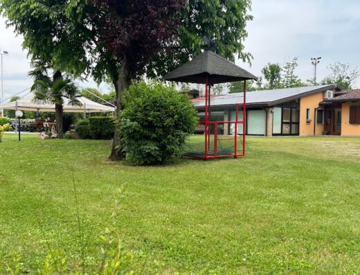 Esterno dell'Agriturismo Al Buttasella, con prato verde, alberi e una struttura in legno rossa, ideale per un soggiorno rilassante.