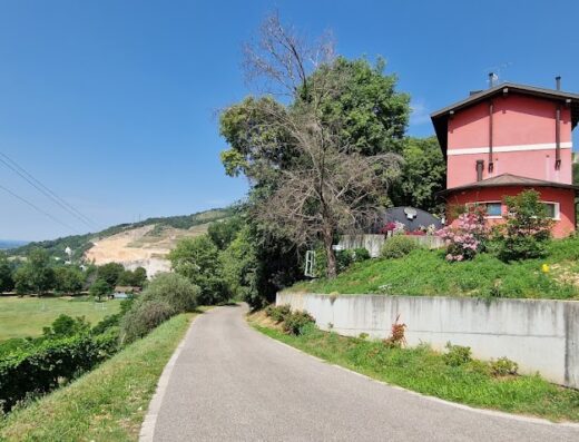 Strada di campagna che conduce all'Agriturismo al Pisoler, con vista panoramica sulla valle e una casa colonica rossa immersa nel verde.