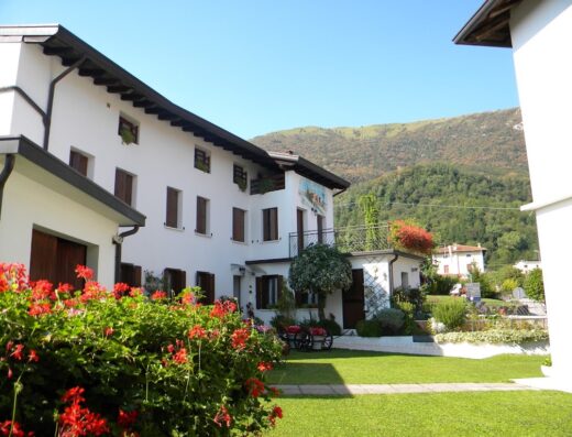 Agriturismo Alle Ruote: Facciata esterna dell'agriturismo con giardino curato, fiori rossi in primo piano e montagne sullo sfondo