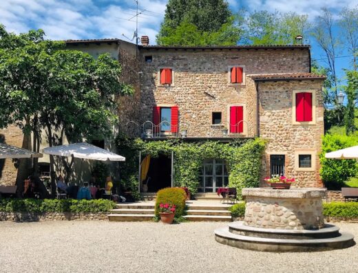 Agriturismo Antica Dimora del Turco: Facciata esterna in pietra con finestre rosse, pozzo decorativo e vegetazione rigogliosa, ideale per un soggiorno rilassante.