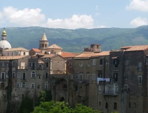 Panorama dell'Agriturismo Antico Pozzo degli Ulivi con vista su un borgo storico italiano, case in pietra, cupola di chiesa dorata e montagne sullo sfondo.