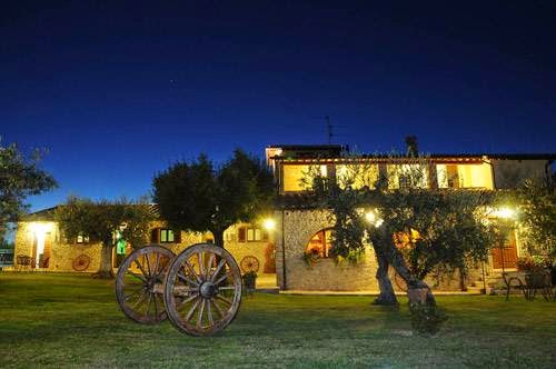 Agriturismo Arcobaleno della Torretta illuminato di sera, con ruote di carro decorative nel prato.