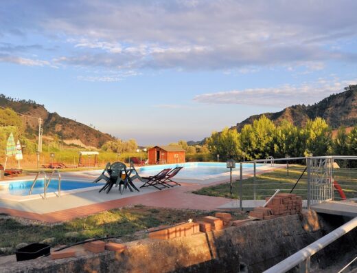 Agriturismo A'Sena-Runcatini: Vista panoramica delle piscine con sedie a sdraio, tavoli e capanno in un paesaggio collinare.