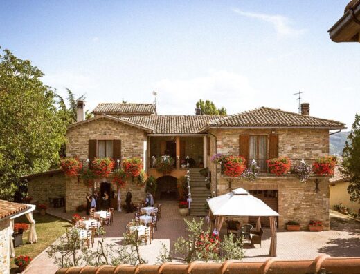 Agriturismo Aurora a Gubbio, Umbria: vista esterna della struttura in pietra con tavoli all'aperto per cene e eventi.