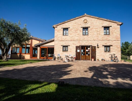 Agriturismo B&B Cadabò: Veduta esterna della struttura in mattoni con bicicletta appoggiata, tavolino con sedie, prato verde e albero di ulivo.