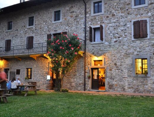 Agriturismo Borgo Floreani: Facciata in pietra con persone sedute ai tavoli esterni, atmosfera accogliente per un soggiorno rilassante.