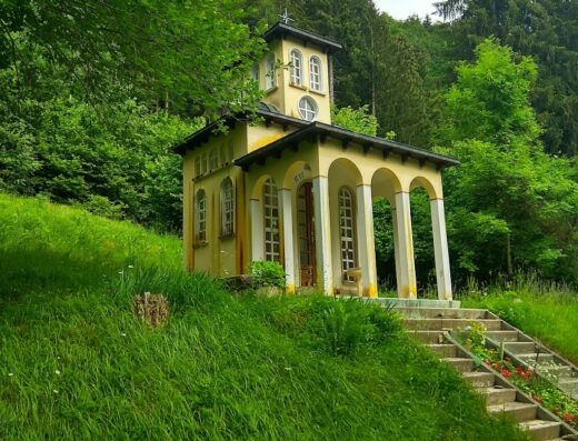 Agriturismo Bosco di Museis: A quaint, yellow building with white columns and windows, nestled on a grassy hill surrounded by lush green trees.