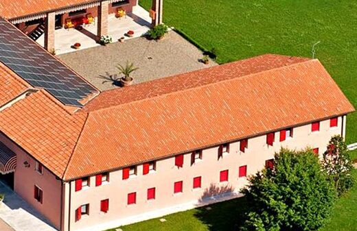 Agriturismo Cà Amedeo vista dall'alto, mostrando la struttura con tetto in tegole rosse, pannelli solari e prato verde circostante.