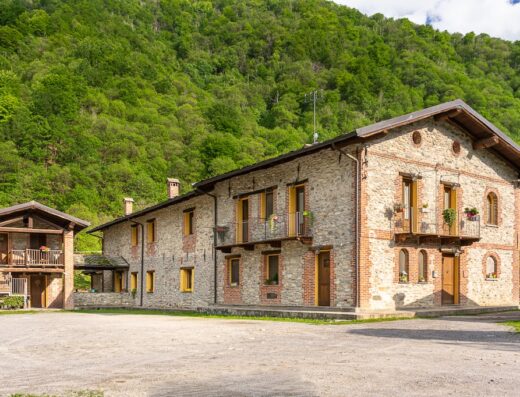 Agriturismo Cascina Veja: Exterior view of the stone farmhouse with small balconies and a lush green hillside backdrop.
