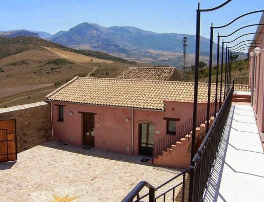 Agriturismo Case Tabarani vista esterna con casa rurale, tetto di tegole, muri rosa, pavimentazione in pietra e panorama montano