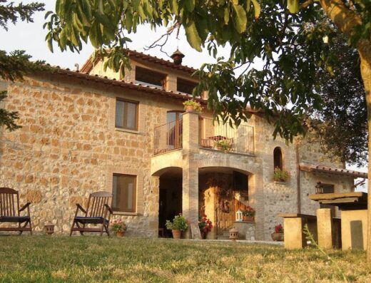 Agriturismo Cioccoleta: Charming stone farmhouse with balcony, two wooden chairs on the lawn, and rustic outdoor seating area.