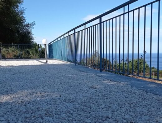 Terrazza panoramica all'Agriturismo Codula Fuili con vista mare attraverso la ringhiera blu, pavimentata con ghiaia bianca.