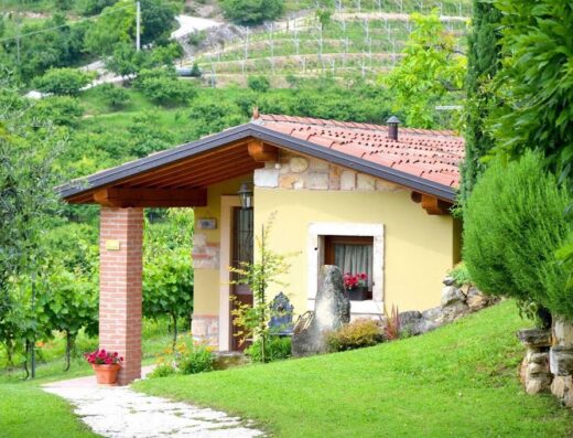 Agriturismo Corte Tamellini: Charming yellow country house nestled in a green landscape with vineyards in the background, offering a tranquil travel destination.