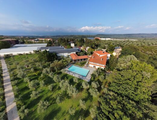 Agriturismo Costantino aerial view featuring olive groves, solar panels, swimming pool, and buildings under a blue sky in Italy.