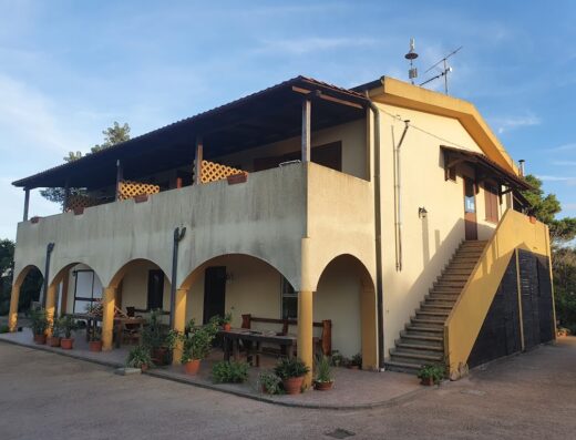 Agriturismo Cuile de Molino, Sardegna: Facciata esterna dell'agriturismo con archi, balcone coperto, scala esterna e tavoli all'aperto.