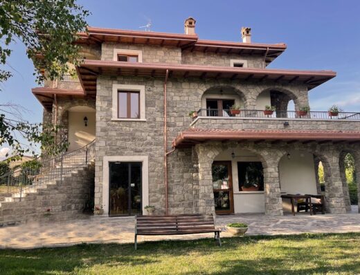 Agriturismo Cupello: Esterno di una casa in pietra su più livelli con balconi ad arco, tetto in legno e giardino curato.
