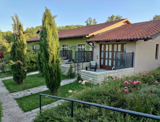 Esterno dell'Agriturismo da Mamma con giardino curato, piante di cipresso, fiori rosa e terrazze private arredate.