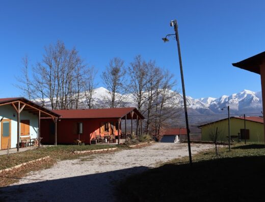 Agriturismo D'Apostolo view of cozy cabins with snow-capped mountains in the background, a tranquil travel destination.