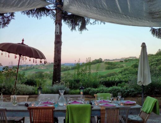 Tavolo imbandito all'Agriturismo Due Papaveri con vista sulle colline toscane, ombrellone decorativo e atmosfera accogliente per una cena indimenticabile.