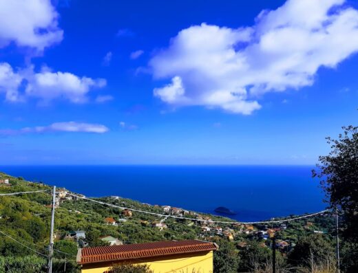 Panoramica mozzafiato dal Agriturismo Le Tore, con vista sul mare cristallino, il borgo collinare e il cielo azzurro costellato di nuvole bianche.