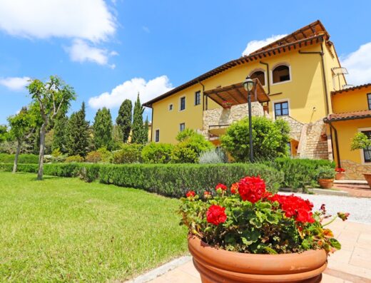 Agriturismo eco-bio Belmonte Vacanze: Vista esterna della struttura con giardino curato, fiori rossi in vaso e cielo azzurro.